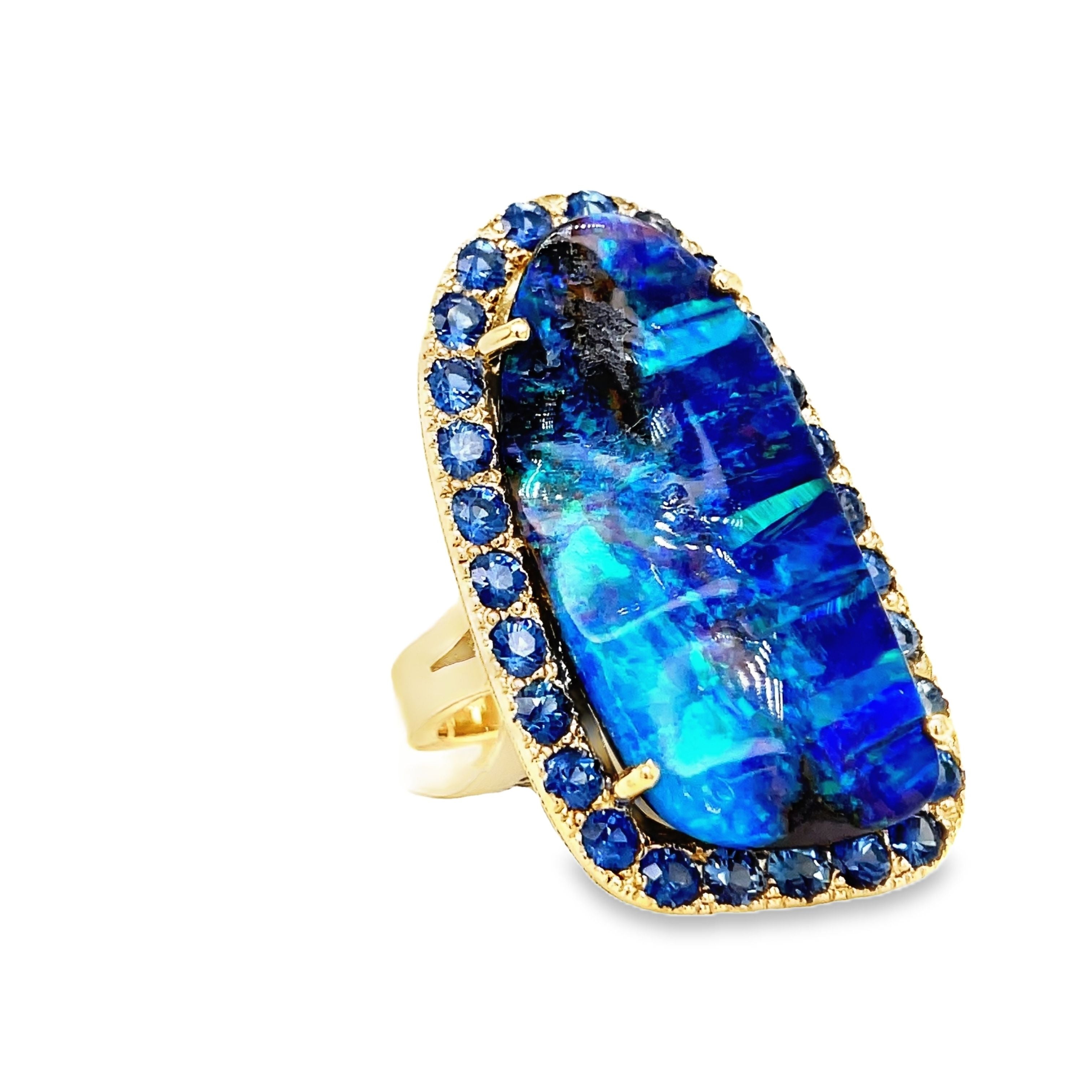 Indulge in elegance with our Hand Made Large Australian Black Opal and Sapphire Ring. Crafted with 14k yellow gold, the stunning 18.00 ct opal boasts a mesmerizing play of color. Adorned with 3.00 ct round sapphires, this piece is a true work of art.