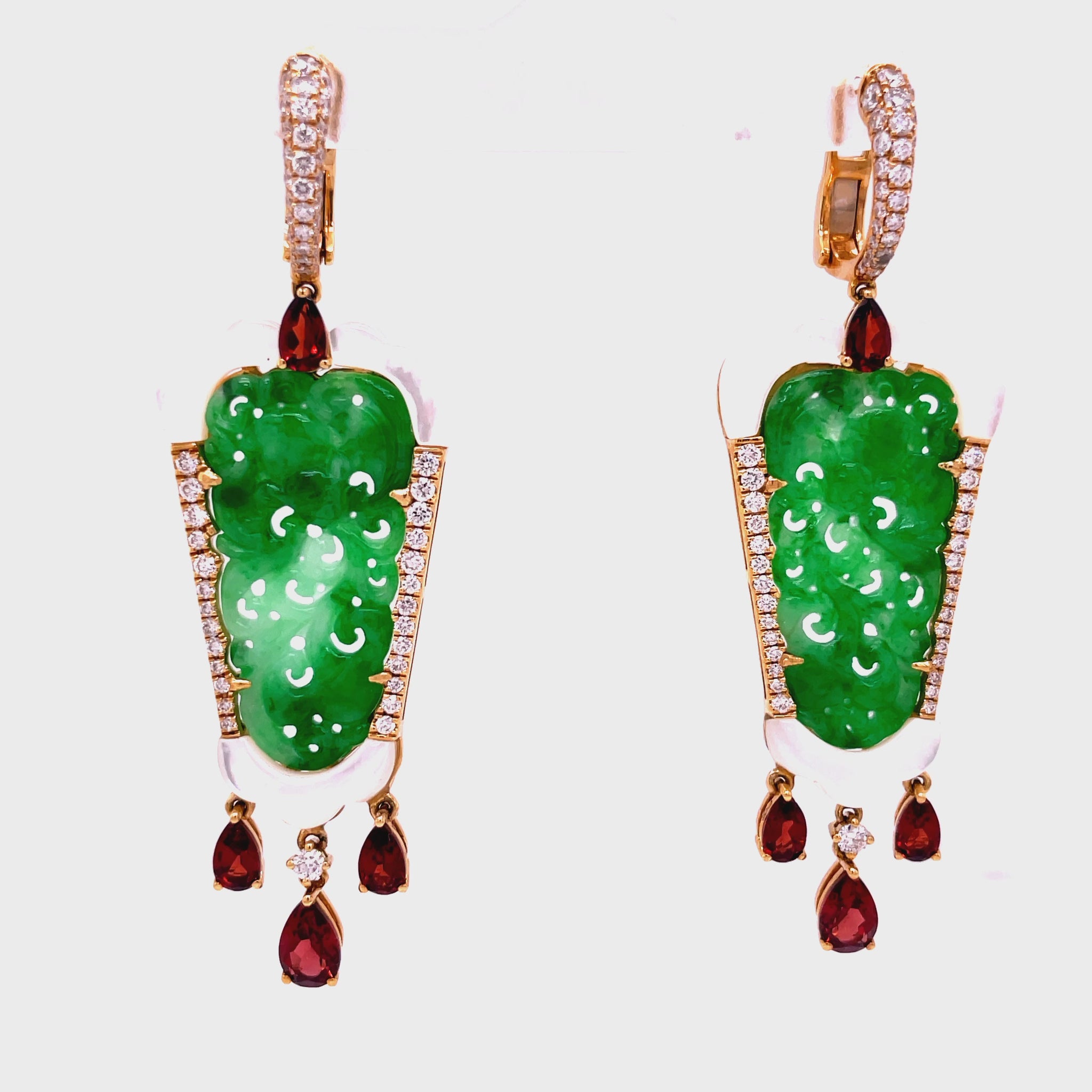 Elevate your style with these stunning green jade earrings hand carved with mother pearl and dazzling round diamonds. The dangling pear shape garnets add a touch of elegance to this 18k yellow gold design. With a secure huggie system, these earrings are 2.5" long. Own a piece of art that will make you stand out.