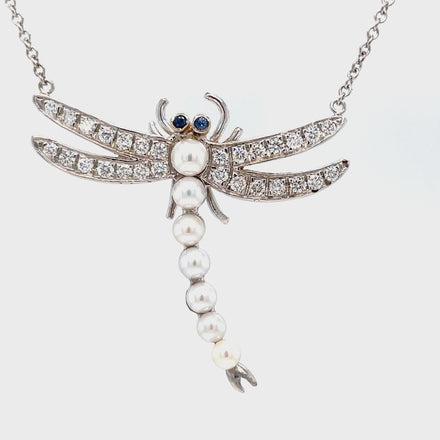 Unleash your inner elegance with our custom-made Diamond & Pearl Dragonfly Pendant Necklace! This stunning pendant features sparkling round diamonds totaling 0.98 carats, delicately arranged on a dragonfly design. Adorned with 7 cultured pearls and set on an 18" white gold chain, this pendant hangs at 1.5 inches long and wide. Elevate any outfit with this exquisite piece!