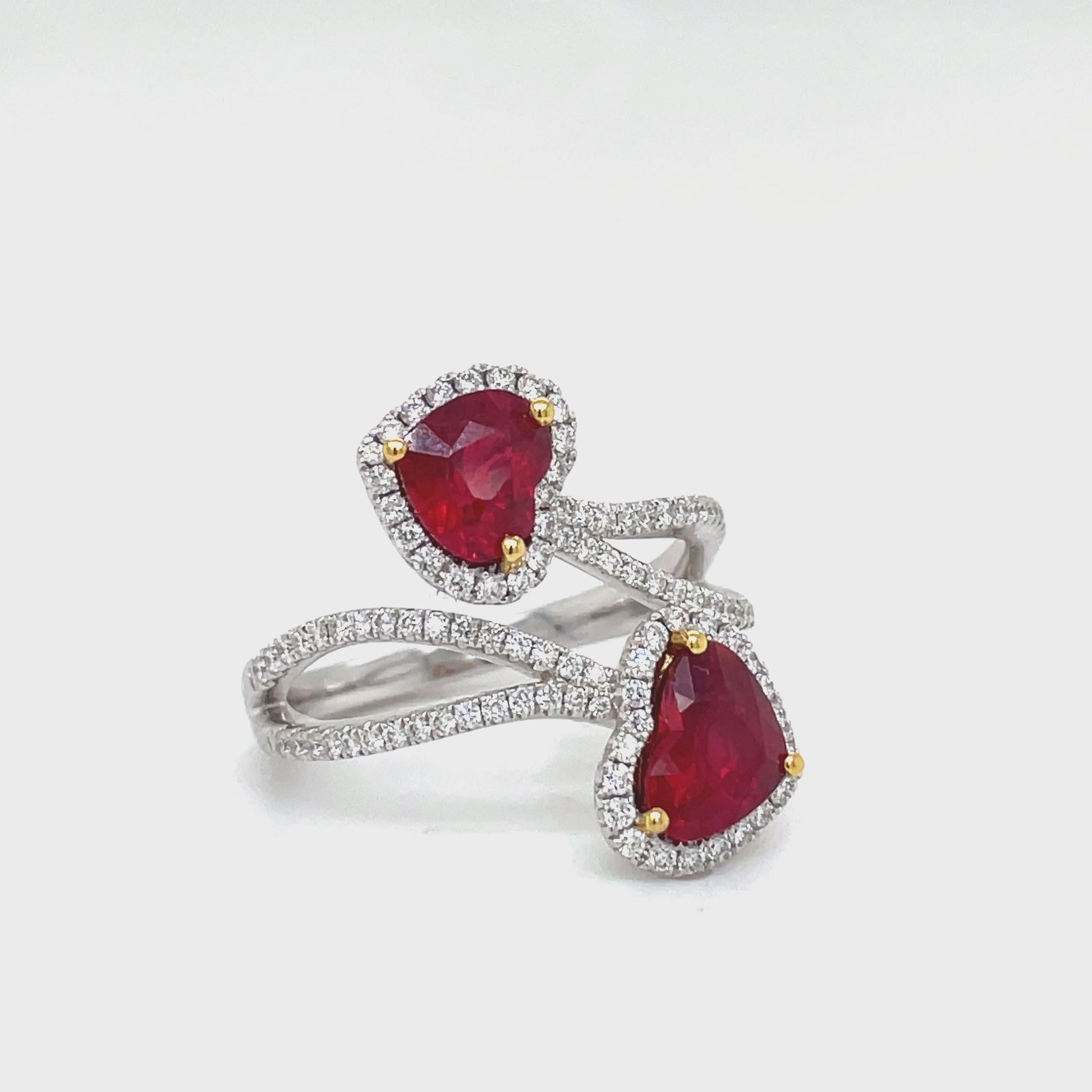 Indulge in luxury with our Heart Shape Rubies and Diamond Crossover Ring. Crafted from 18k white gold, this ring features two heart-shaped rubies totaling 2.33 carats and sparkling round diamonds totaling 0.47 carats. The perfect symbol of love and elegance.