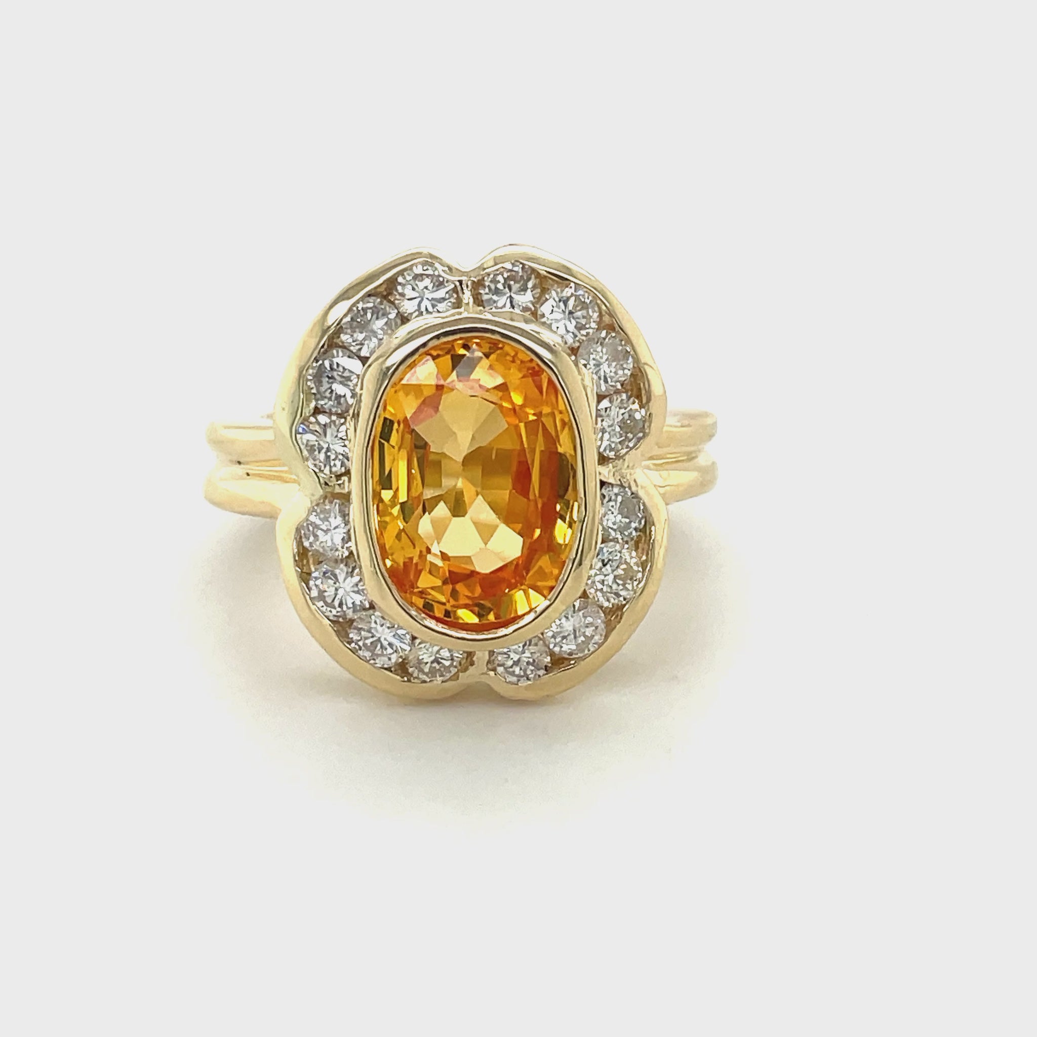 This stunning ring features an orange-yellow oval sapphire of 4.11 carats, surrounded by white round diamonds of 0.93 carats in total weight. Set in 14K white gold, this one-of-a-kind piece guarantees a high-quality craftsmanship and will be a unique addition to any jewelry collection. The ring is 18.00 mm in size and 15.00 mm in width.