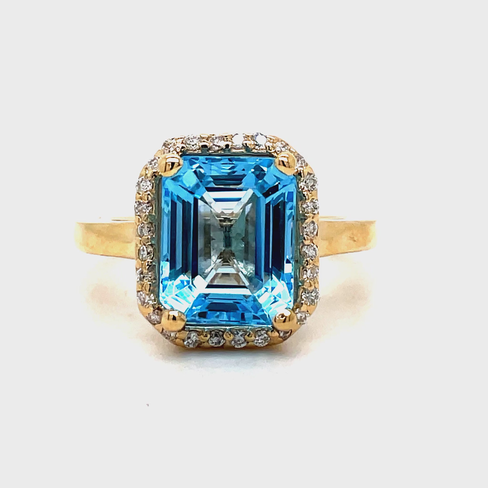 Indulge in the exquisite elegance of this Emerald Cut Blue Topaz Diamond Halo Ring. Crafted in 14k yellow gold, the cathedral style setting highlights a stunning emerald cut Blue Topaz, surrounded by sparkling round diamonds totaling 0.40 carats. A true masterpiece, perfect for any sophisticated and exclusive individual.