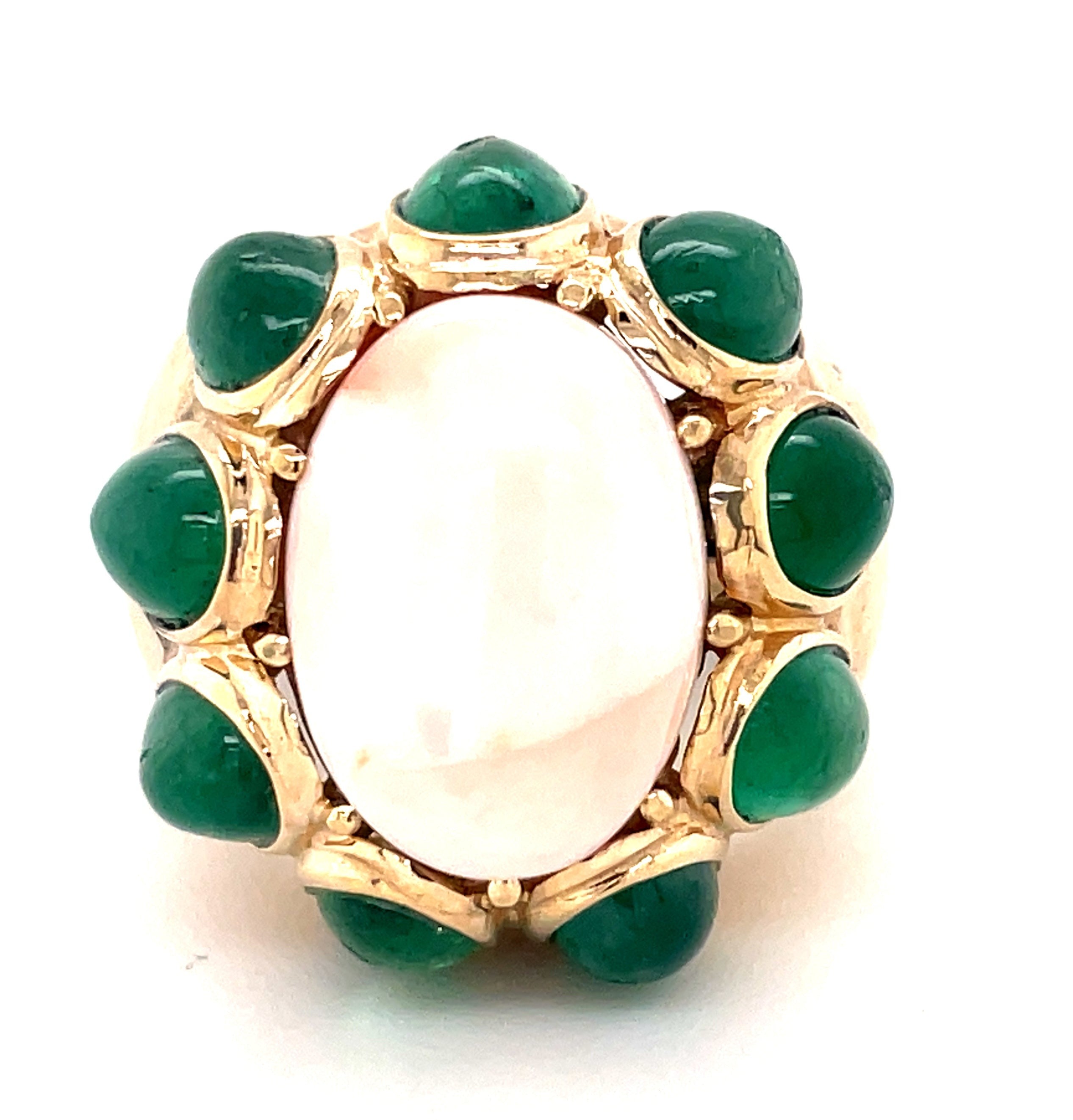 This 14k yellow gold antique ring is a stunning example of estate jewelry, with an angel skin coral cabochon measuring 23.00 mm surrounded by nine large emerald cabochons. Its great condition will make it a timeless piece you can treasure for years to come.