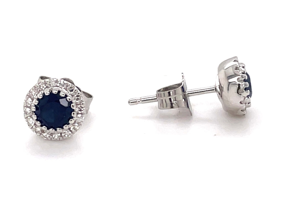 This pair of earrings features a blue sapphire center of 0.81 carats, enhanced by 0.11 carats of round white diamonds. The stones are set in a 14K white gold bezel setting and are secured with friction backs measuring 6.50 mm.