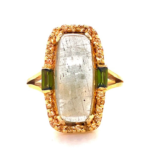 One rectangular cabochon milky aquamarine 20.00 x 12.00 mm 4.95 cts  Bezel set round yellow sapphires 0.20 cts   Square green tourmalines 0.95 cts  Set in 14k yellow gold  Open shank yellow band