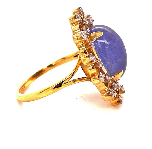 One round tanzanite cabochon 14.00 x 10.00 mm 5.80 cts  Crowned with a diamond gallery around the tanzanite  Round diamonds 0.48 cts  Set in 14k yellow gold  Open shank yellow band