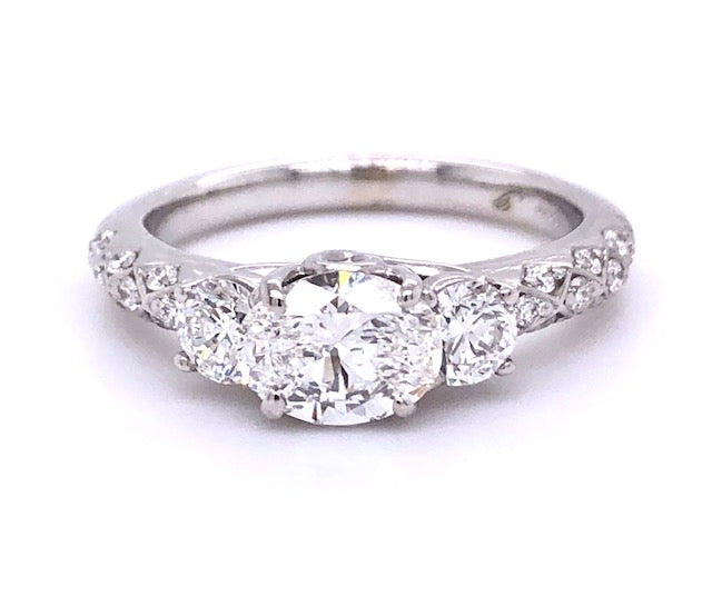 This East-West setting is an unconventional setting that is gaining popularity. This type of setting highlights the wedding band. Comfort is also a great benefit from this style..  GIA certified Oval cut diamond 0.98 cts  Color F  Clarity SI2  Set in 18k white gold contemporary mounting with two round diamonds for side stones 0.40 cts. Matching band 18k white gold adorned with filigree style 0.90 cts total  